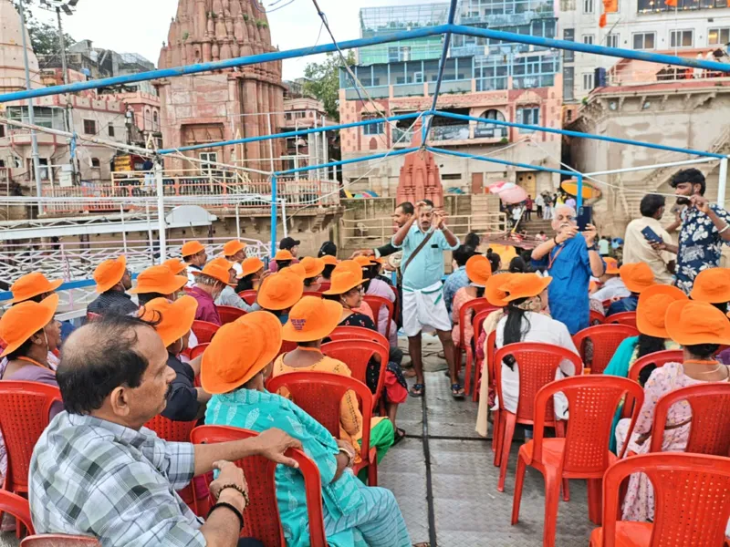 Travellers in orange hats seated on a boat along the Varanasi ghats