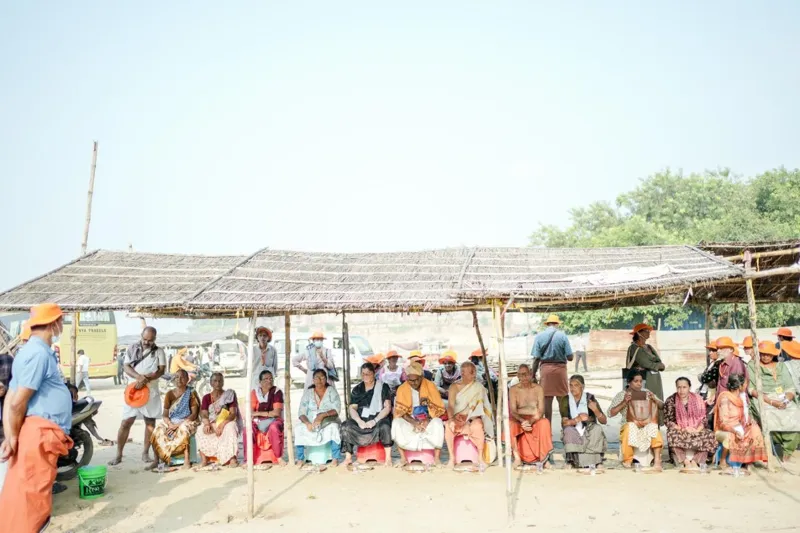 Travellers resting under a thatched shelter on the sandy riverbank